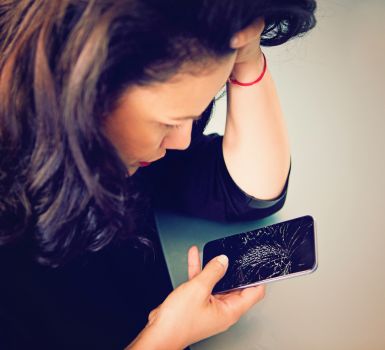 sad woman looking down at broken iphone with cracked screen