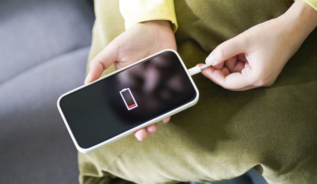 Hands holding a smartphone with a dead battery that won't charge.